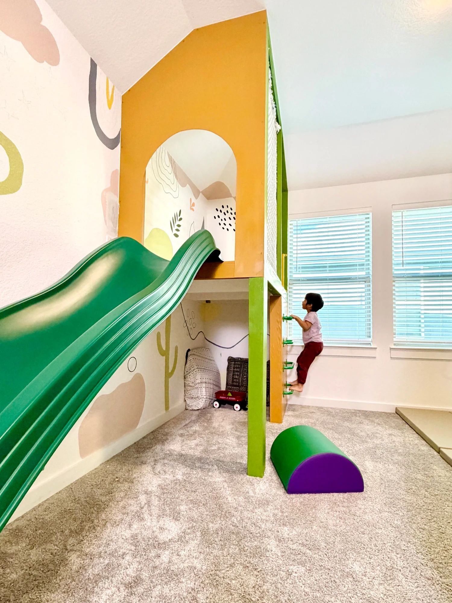 A mustard playhouse with a green slide, and a child climbing the rungs up its side